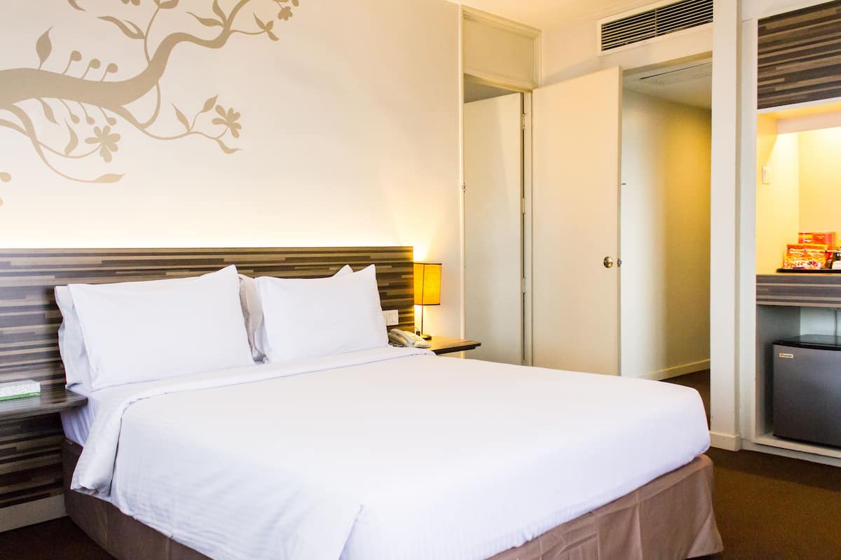 A neatly made bed with white linens, a bedside table with a lamp, and a wall with a floral design.