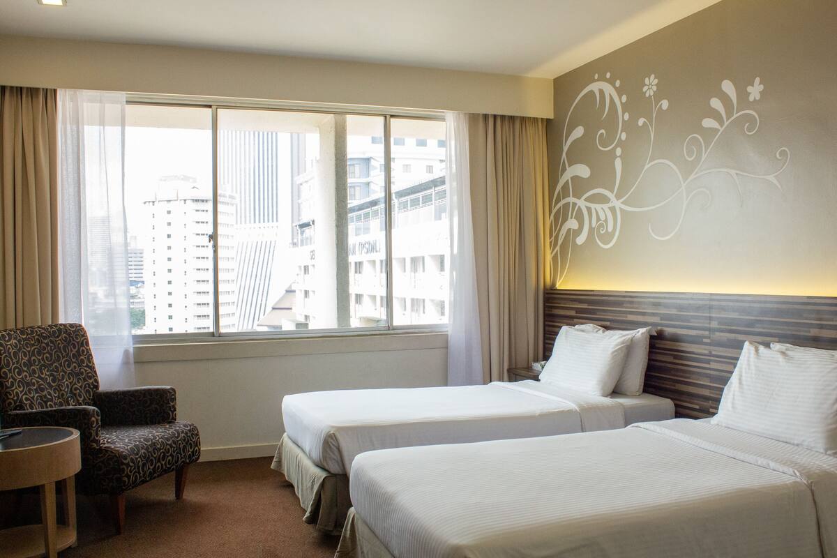 A hotel room with two beds, a chair, and a large window with a city view.