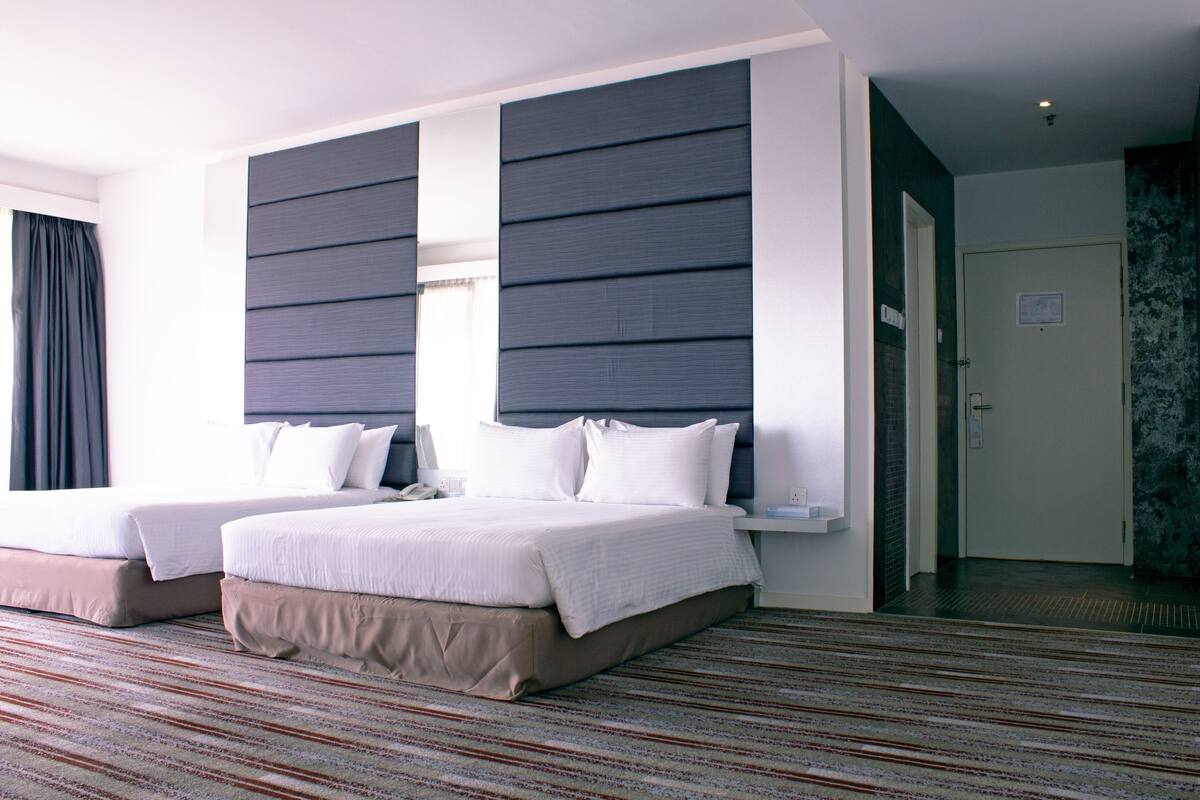 A hotel room with two beds, a striped carpet, and a dark-colored headboard.