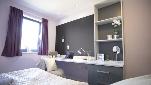 A modern bedroom with a bed, a desk with a laptop, a mirror, and a shelf with decorative items. - Beaverbank Place - Campus Accommodation (Edinburgh)