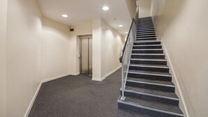 A modern interior with a carpeted hallway, a staircase with metal railings, and a door at the end. - Beaverbank Place - Campus Accommodation (Edinburgh)
