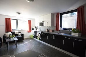 A modern kitchen with black cabinets, a black countertop, and a window with red curtains.