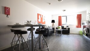 A modern kitchen with a dining area, featuring a bar stool set, a sofa, and a fire extinguisher on the wall. - Beaverbank Place - Campus Accommodation (Edinburgh)
