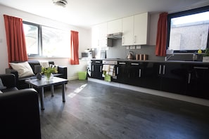 A modern kitchen with black cabinets, a microwave, and a kettle. There is a dining area with a table and chairs.