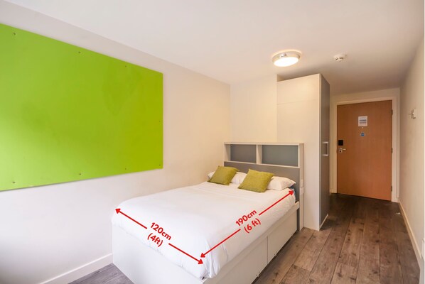 A bedroom with a bed measuring 120cm by 190cm, a green accent wall, and a wooden floor.