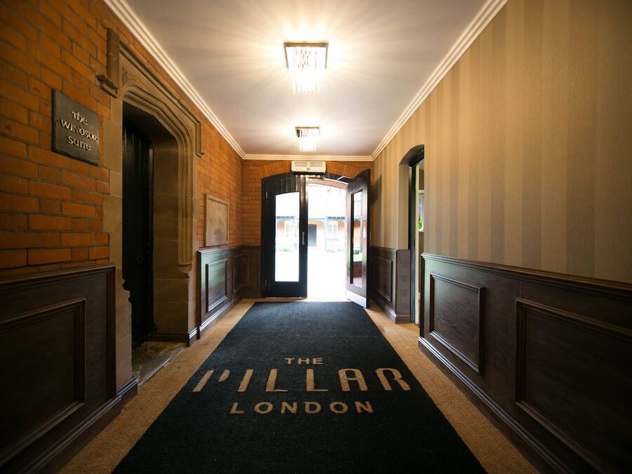 Um corredor com carpete exibindo "The Pillar London" que leva a uma porta.