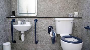 Une salle de bain équipée d’un lavabo, de toilettes et de barres d’appui.