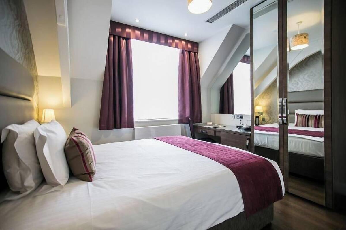 A hotel room with a large bed, a desk, a chair, and a mirror.