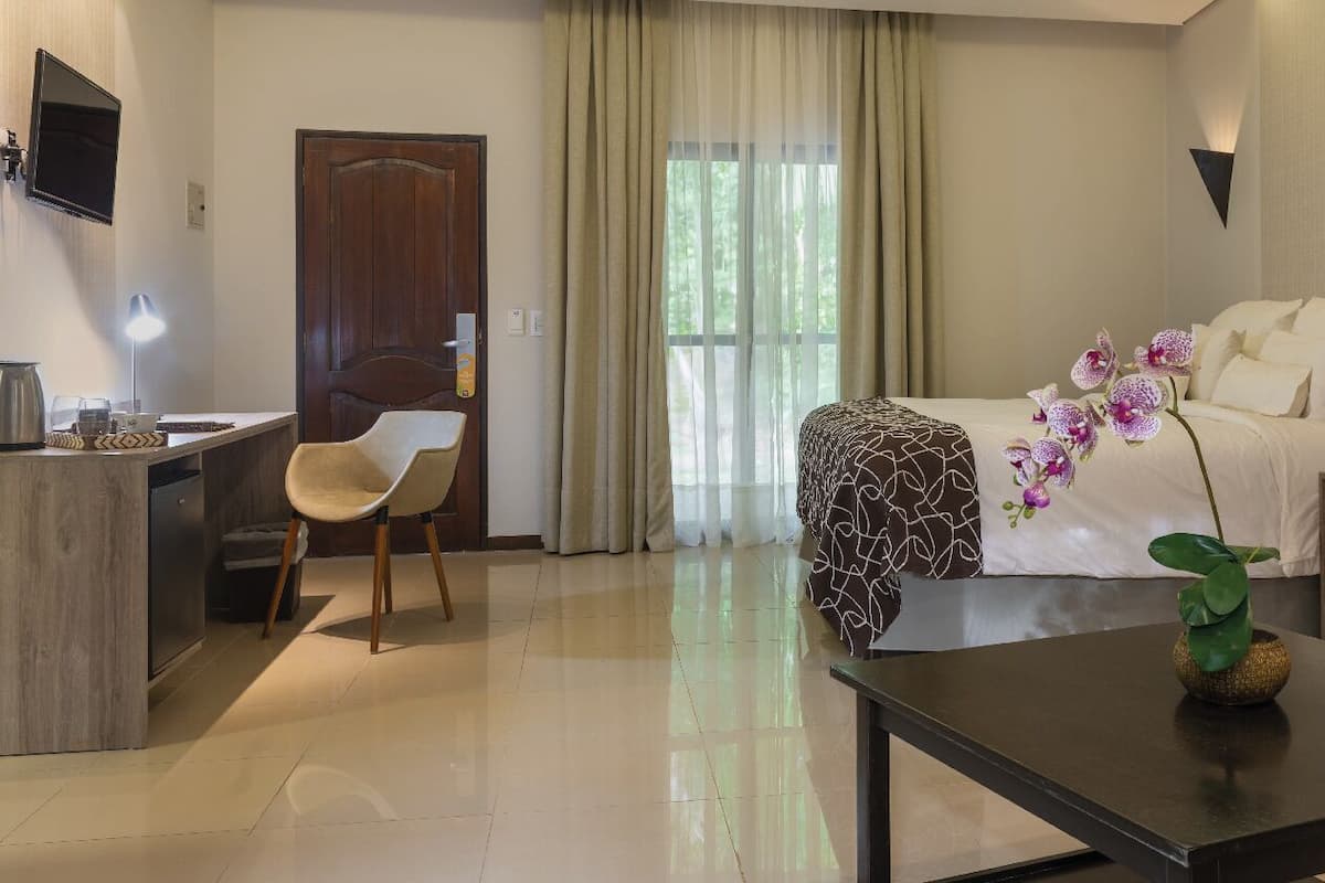Habitación de hotel con cama, escritorio, silla, cafetera y un florero con flores.