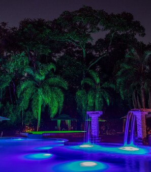 A nighttime outdoor area with illuminated palm trees, a water feature, and a stone structure. - Yvy Hotel de Selva (Puerto Iguazú)