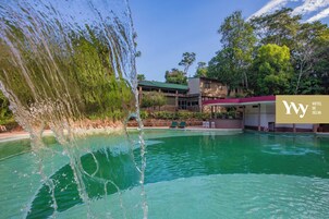Una piscina de hotel con agua cristalina, rodeada de árboles y un edificio con techo verde.