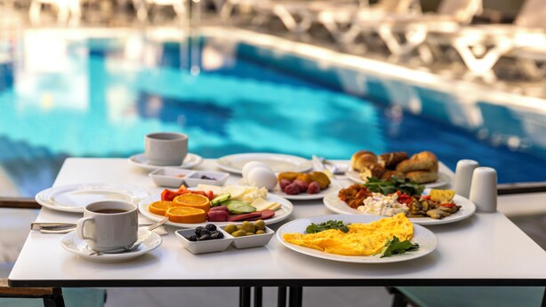 Morgenmadsbuffet med forskellige retter og en pool i baggrunden.