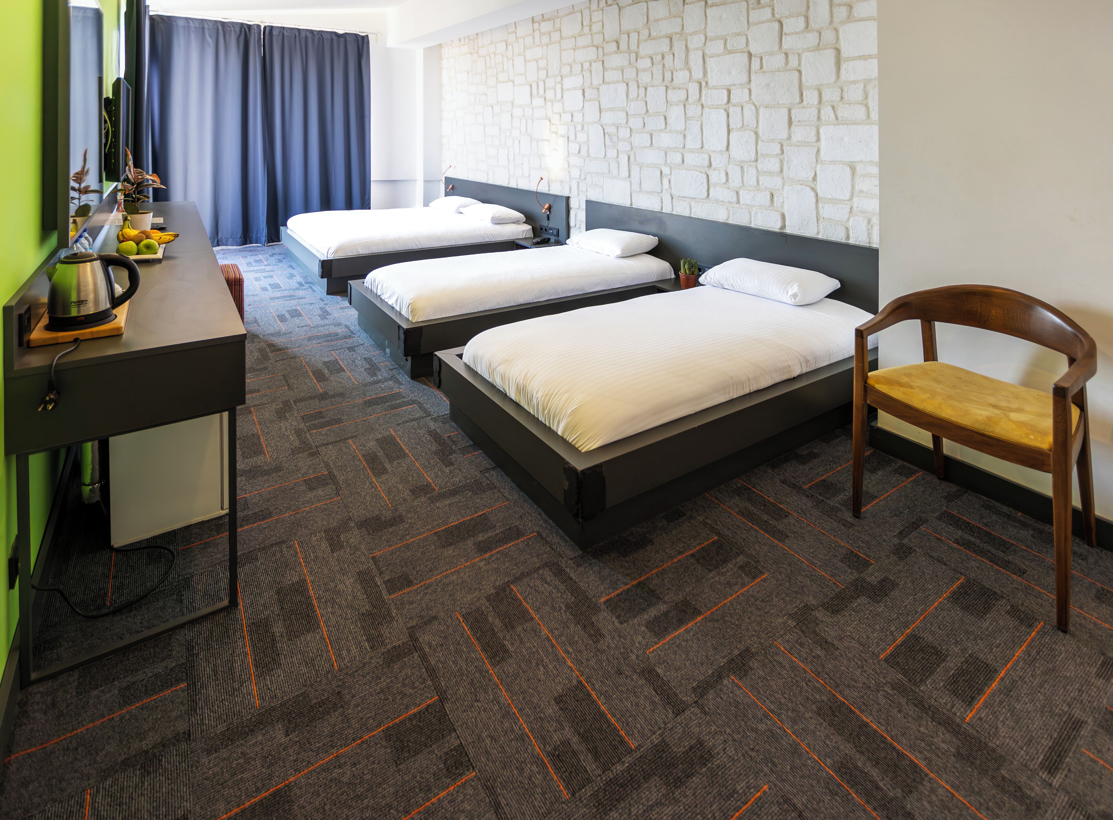 A hotel room with two beds, a desk, a chair, and a wall with a textured pattern.