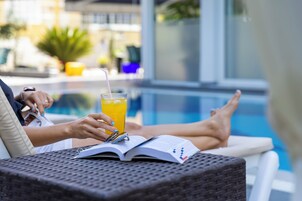 Una persona descansando junto a una piscina, con una bebida y un libro abierto.
