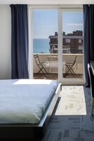 Habitación de hotel con una cama, un pequeño balcón con mesa y sillas, y vista al mar.