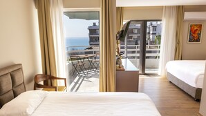 Et hotelværelse med seng, stol, skrivebord og balkon med havudsigt.