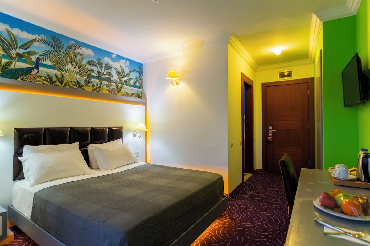 A hotel room with a bed, a dining table with breakfast, a TV, and a door.