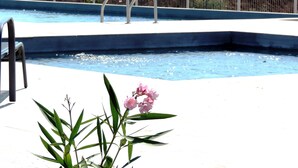 A swimming pool with a white deck, metal pool ladder, and a flower in the foreground.