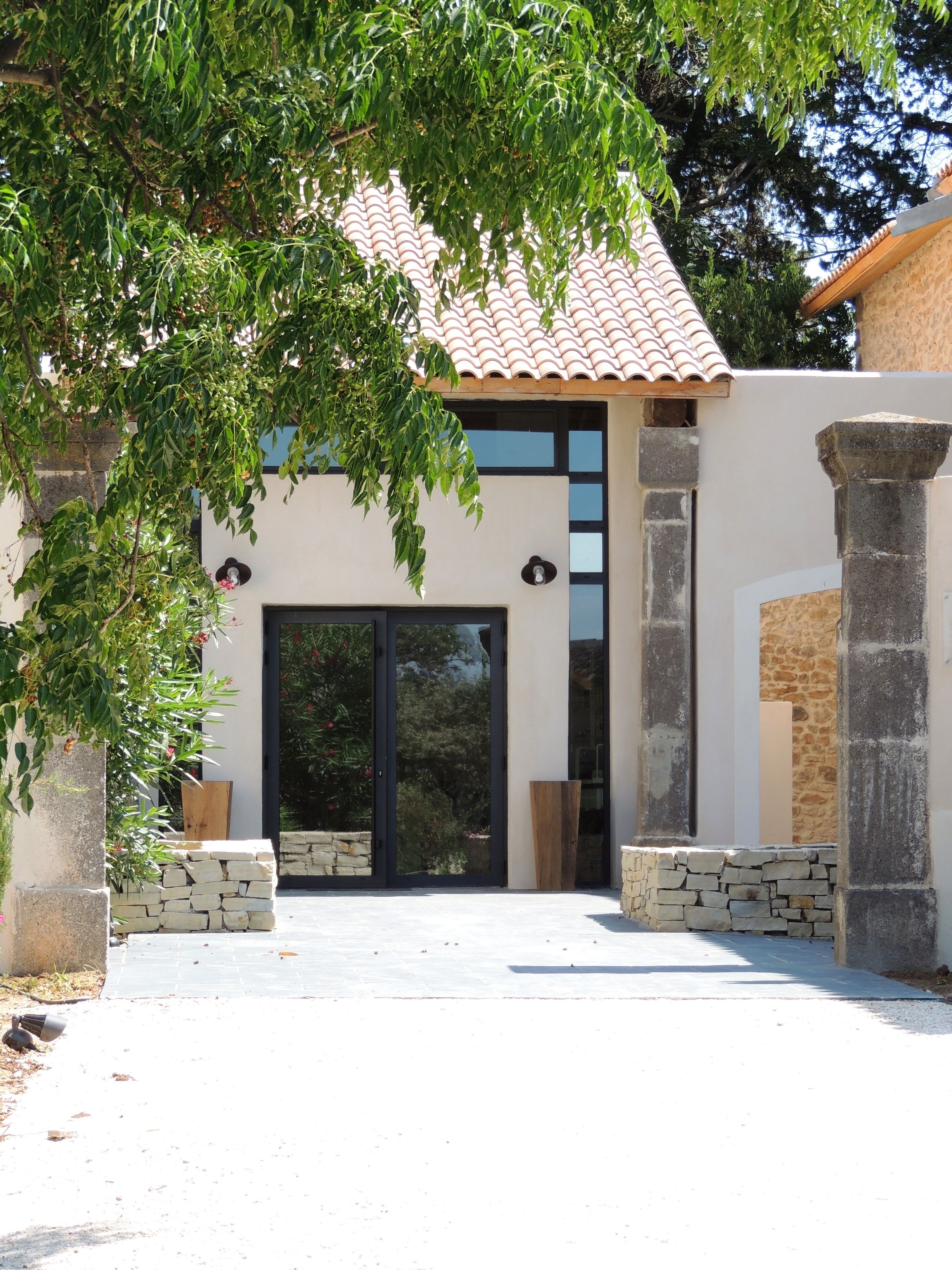 Un edificio moderno con techo de tejas, grandes puertas de cristal, pilares de piedra y un muro de piedra.