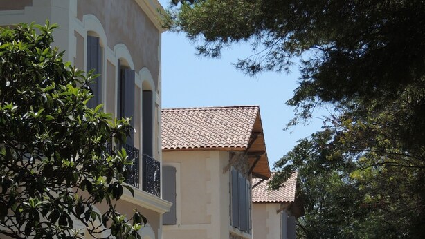 A two-story building with a tiled roof and a garden in front.