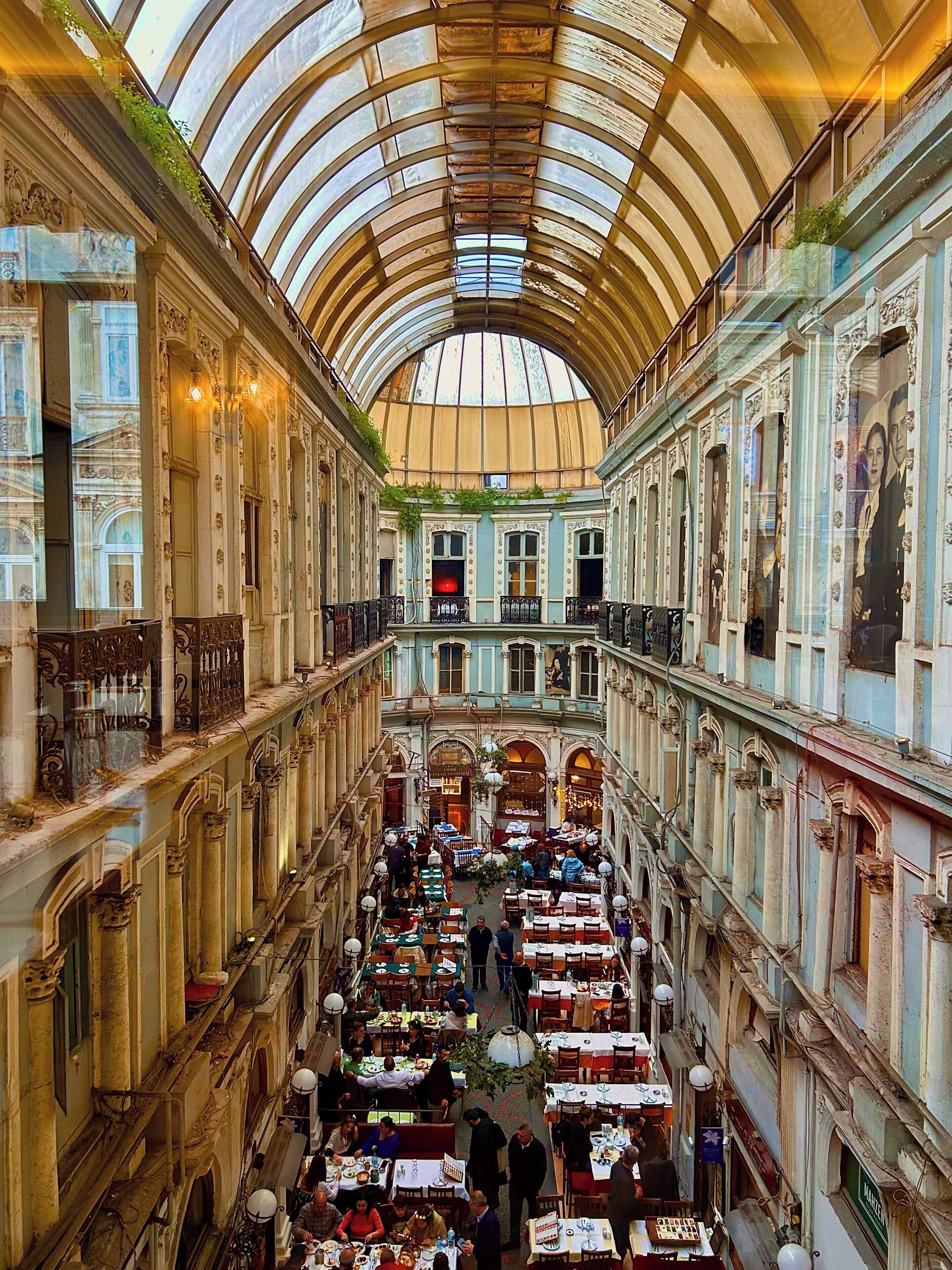 An indoor market with multiple levels, ornate architecture, and a glass ceiling.