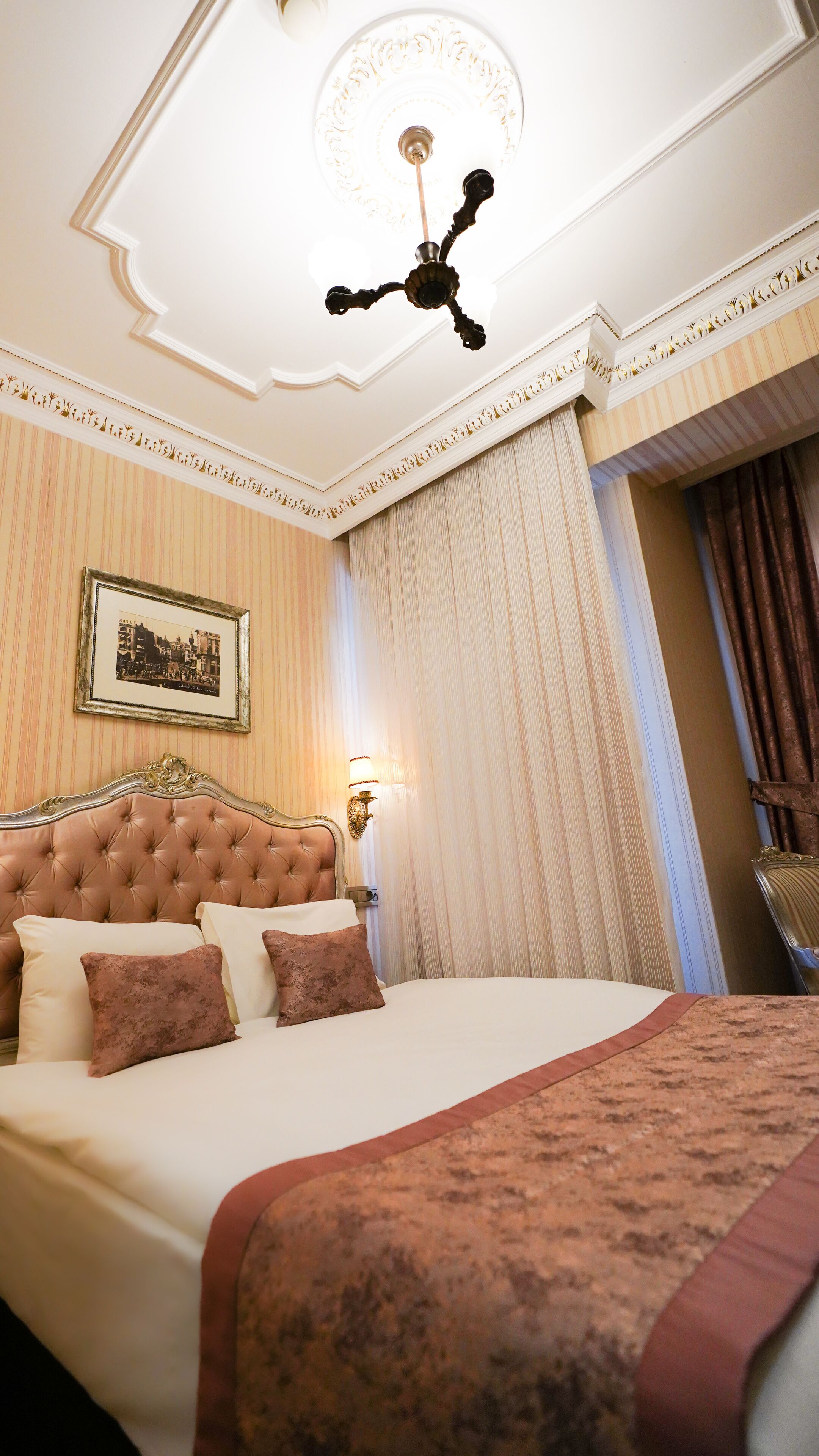 A well-appointed bedroom with a tufted headboard, a large bed with multiple pillows, a wall-mounted picture, and a ceiling light fixture.