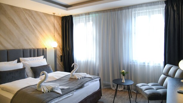 A modern hotel room with a large bed, a comfortable armchair, and a small table. - Hotel zum Weissen Ross (Delitzsch)