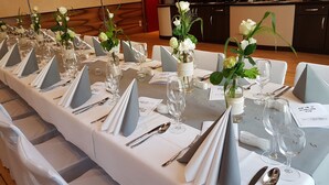 A long dining table set with white tablecloths, grey napkins, and glassware, with vases of flowers and menus. - Hotel zum Weissen Ross (Delitzsch)