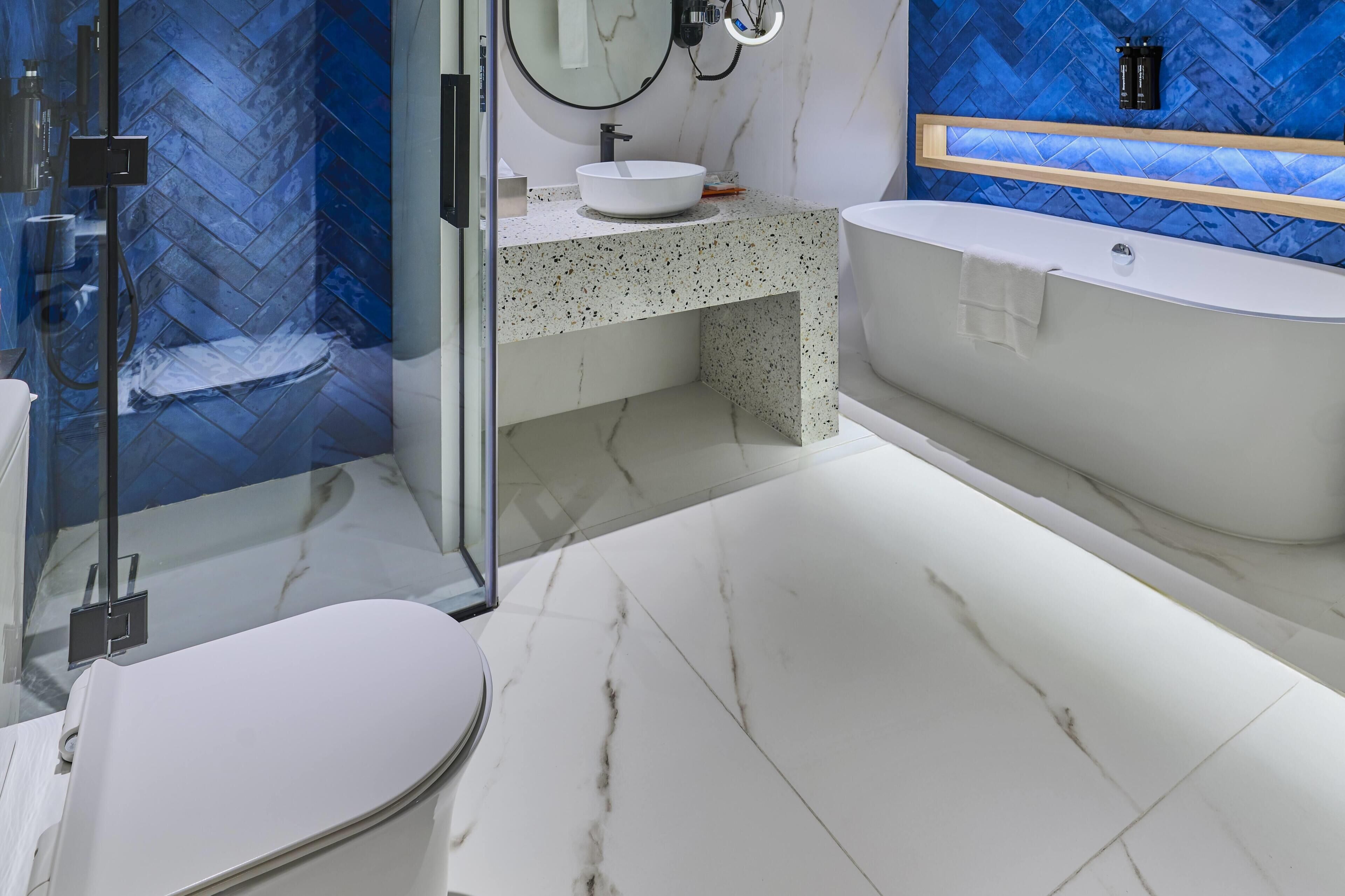 A modern bathroom with a glass shower enclosure, a freestanding bathtub, and a marble-tiled floor.