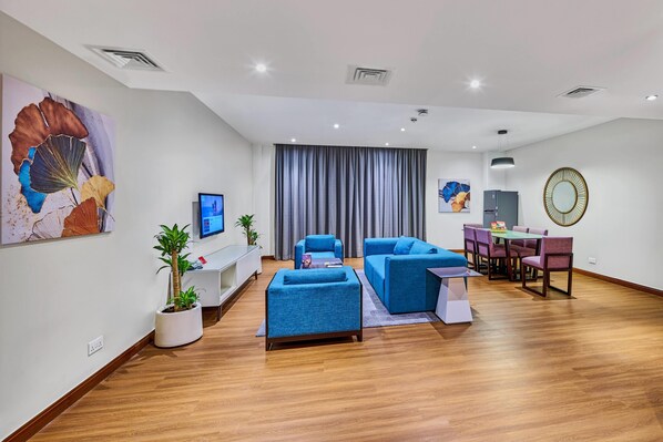Una sala moderna con un televisor de pantalla plana, sofás azules, una mesa de comedor con sillas y una planta en maceta.