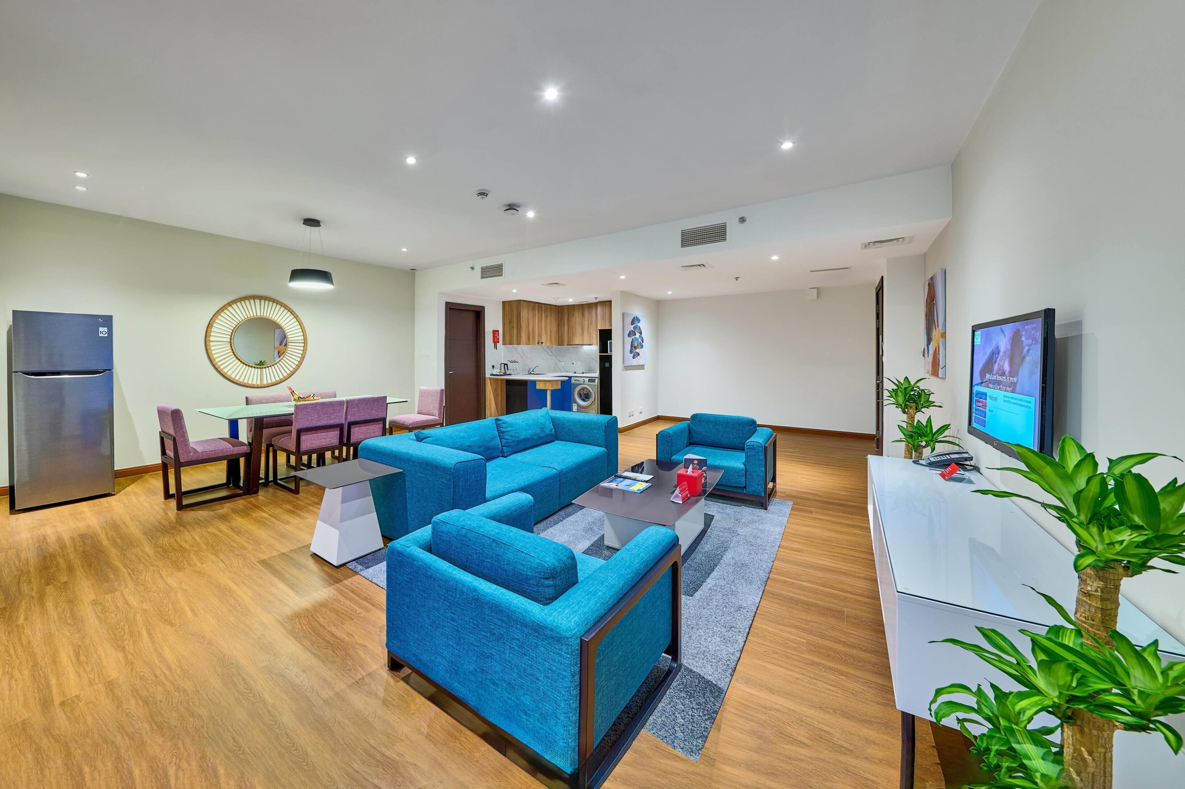 A modern living room with blue sofas, a dining table, and a kitchen area.