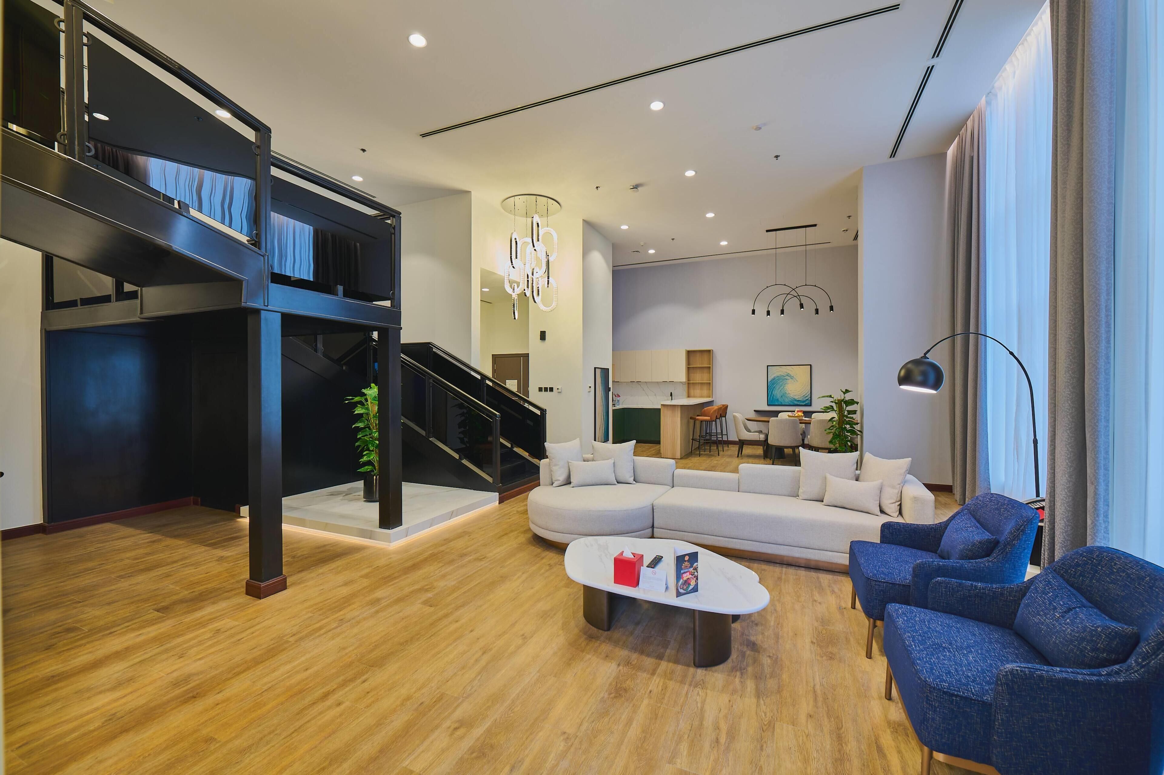 A modern living room with a staircase, a sectional sofa, a coffee table, and a dining area.