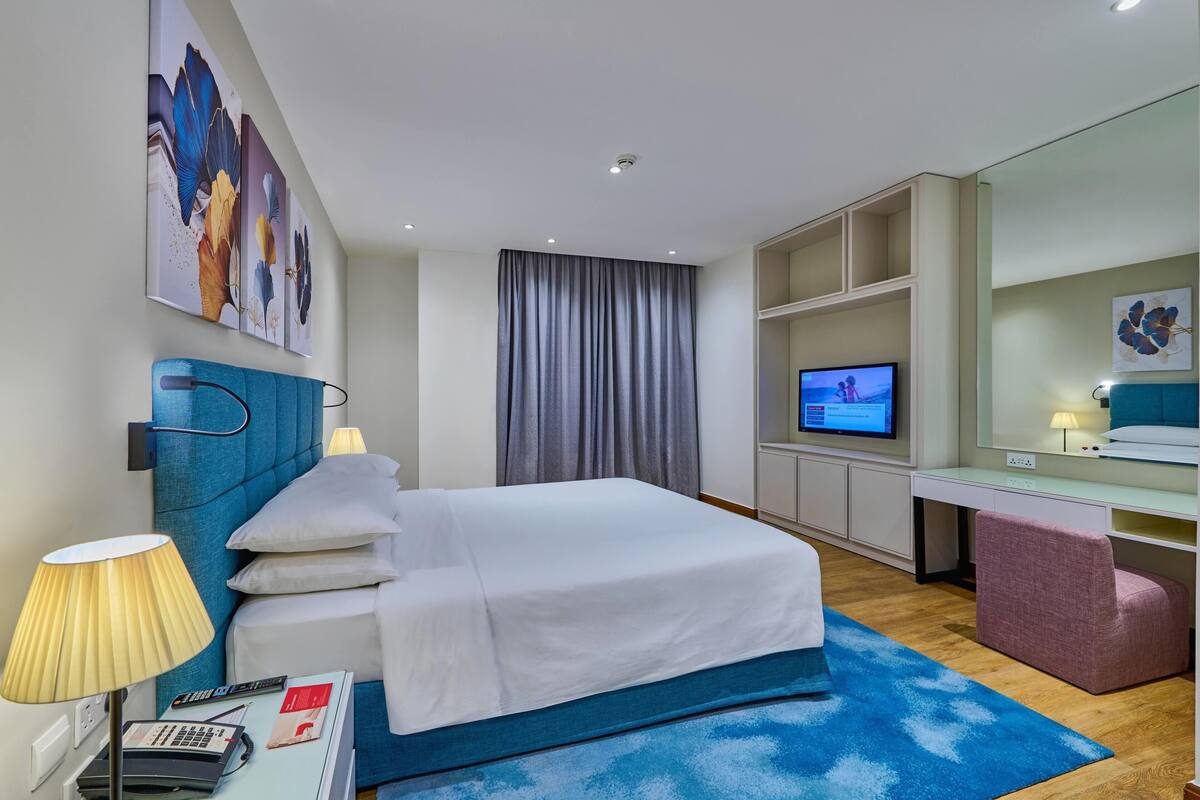 A hotel room with a bed, a desk, a television, and a large window with curtains.