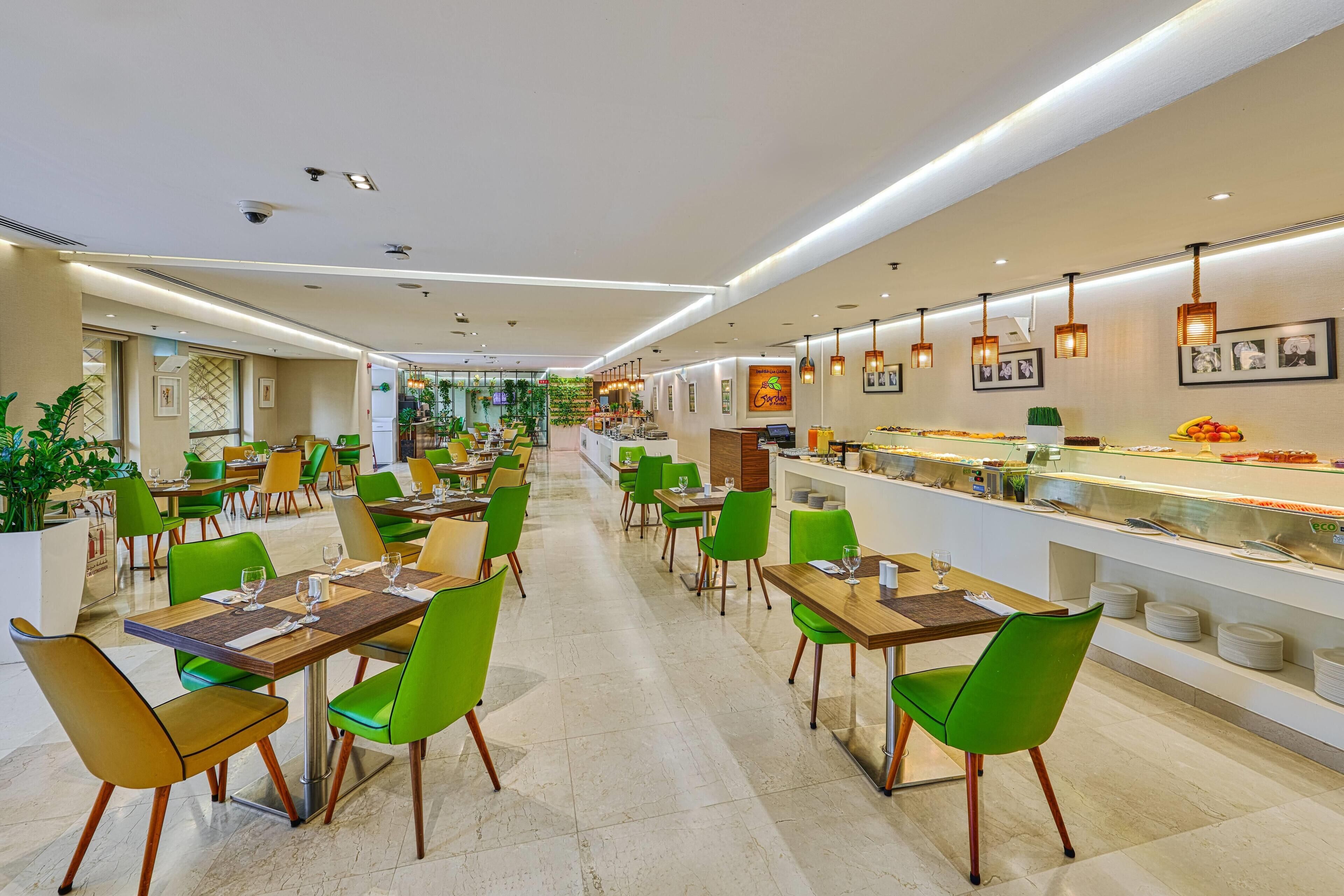 Un restaurant moderne avec des chaises vertes et jaunes, un long comptoir où sont exposés les plats, et un intérieur propre et bien éclairé.