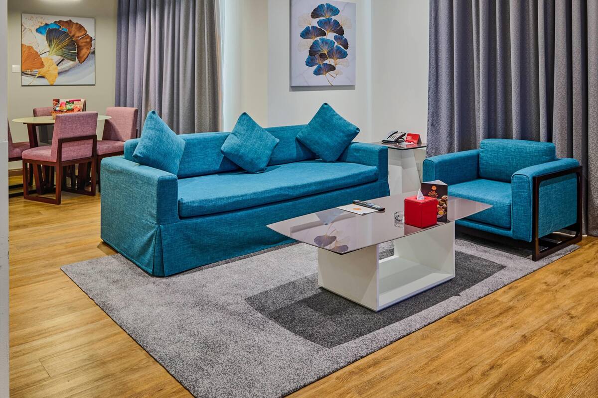 A modern living room with a blue sofa, a glass coffee table, and a dining area with pink chairs.