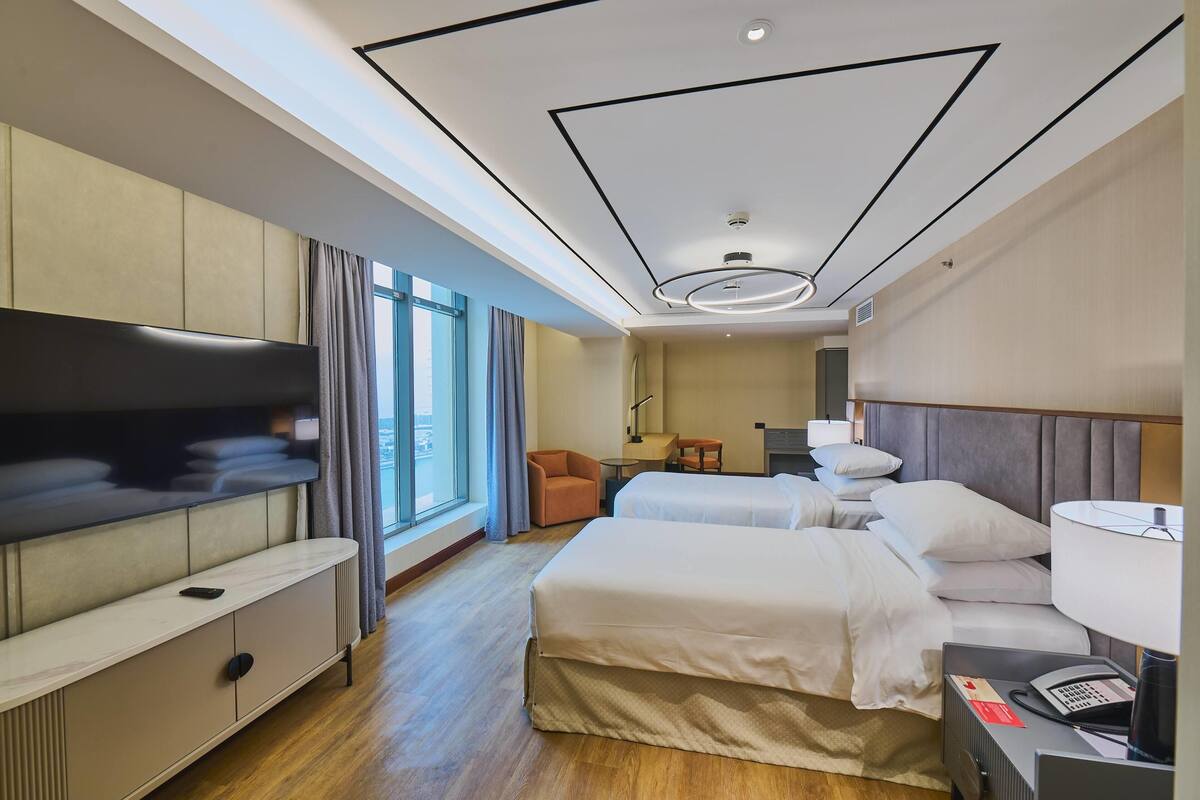 A hotel room with a bed, a desk, a chair, a TV, and a window.