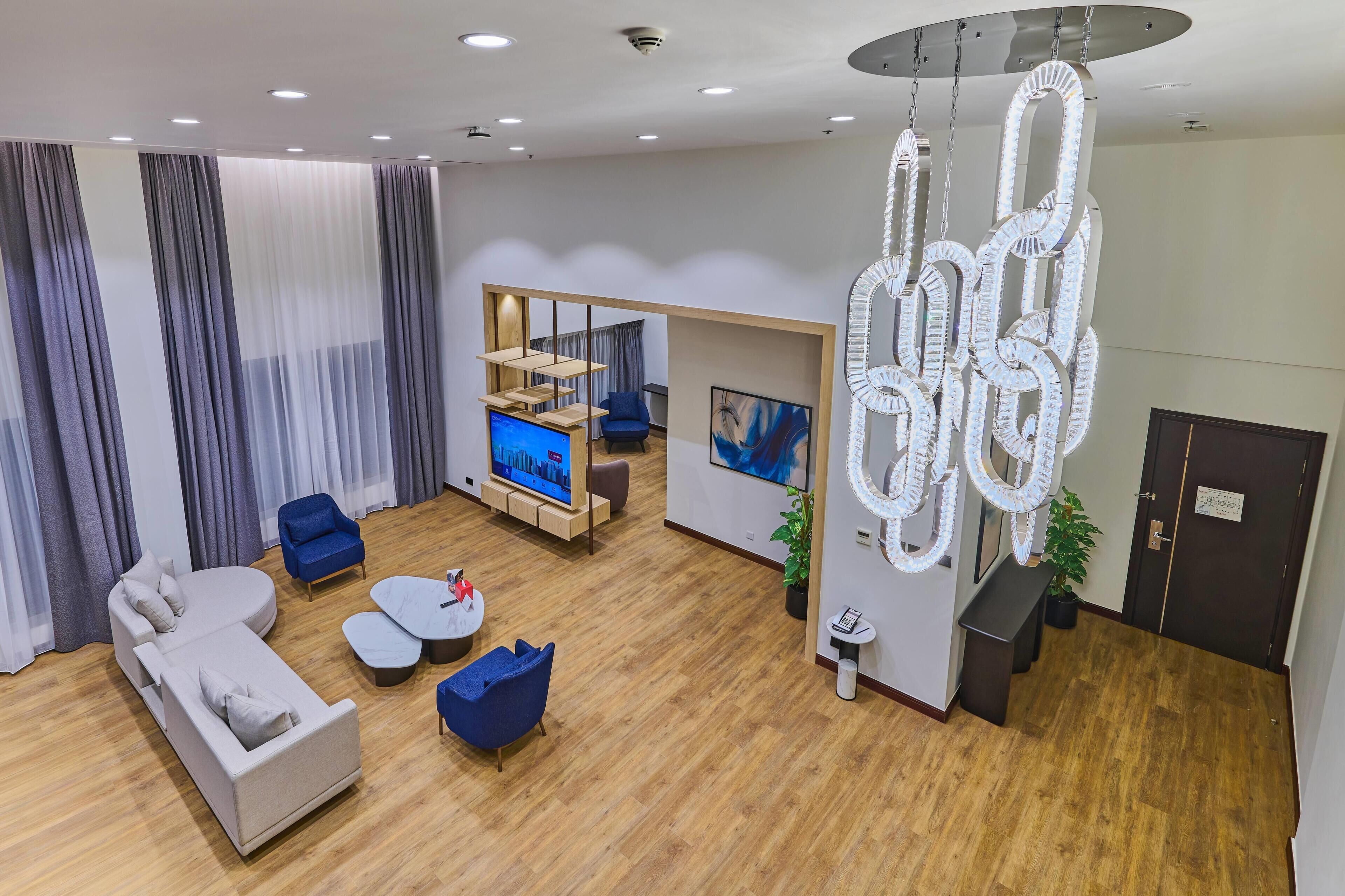 Un salon moderne avec un canapé, des fauteuils, un téléviseur et un lustre original.