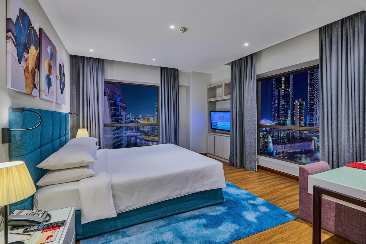A modern hotel room with a large bed, a TV, and a city view.
