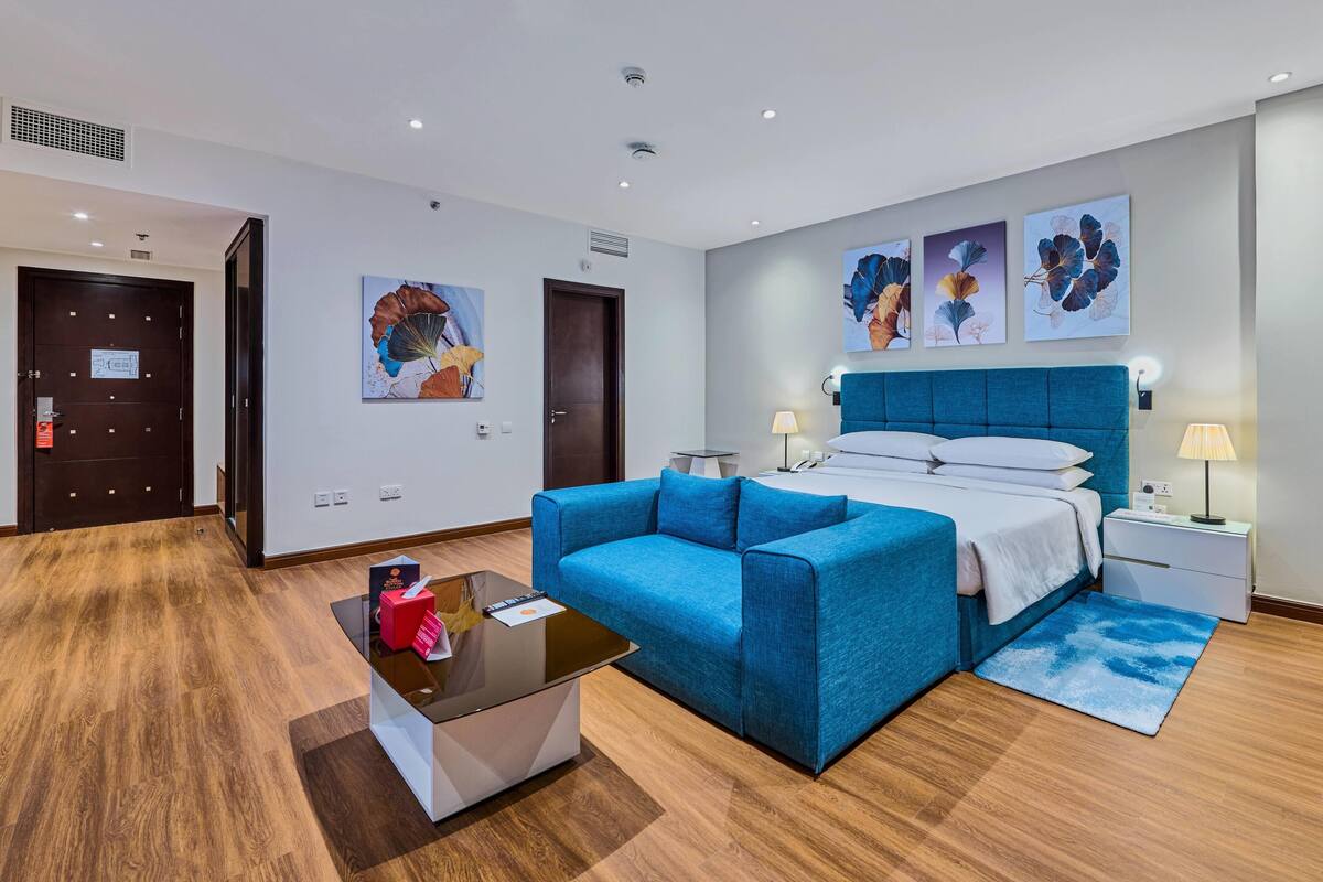 A hotel room with a bed, a blue sofa, a small table, and artwork on the walls.