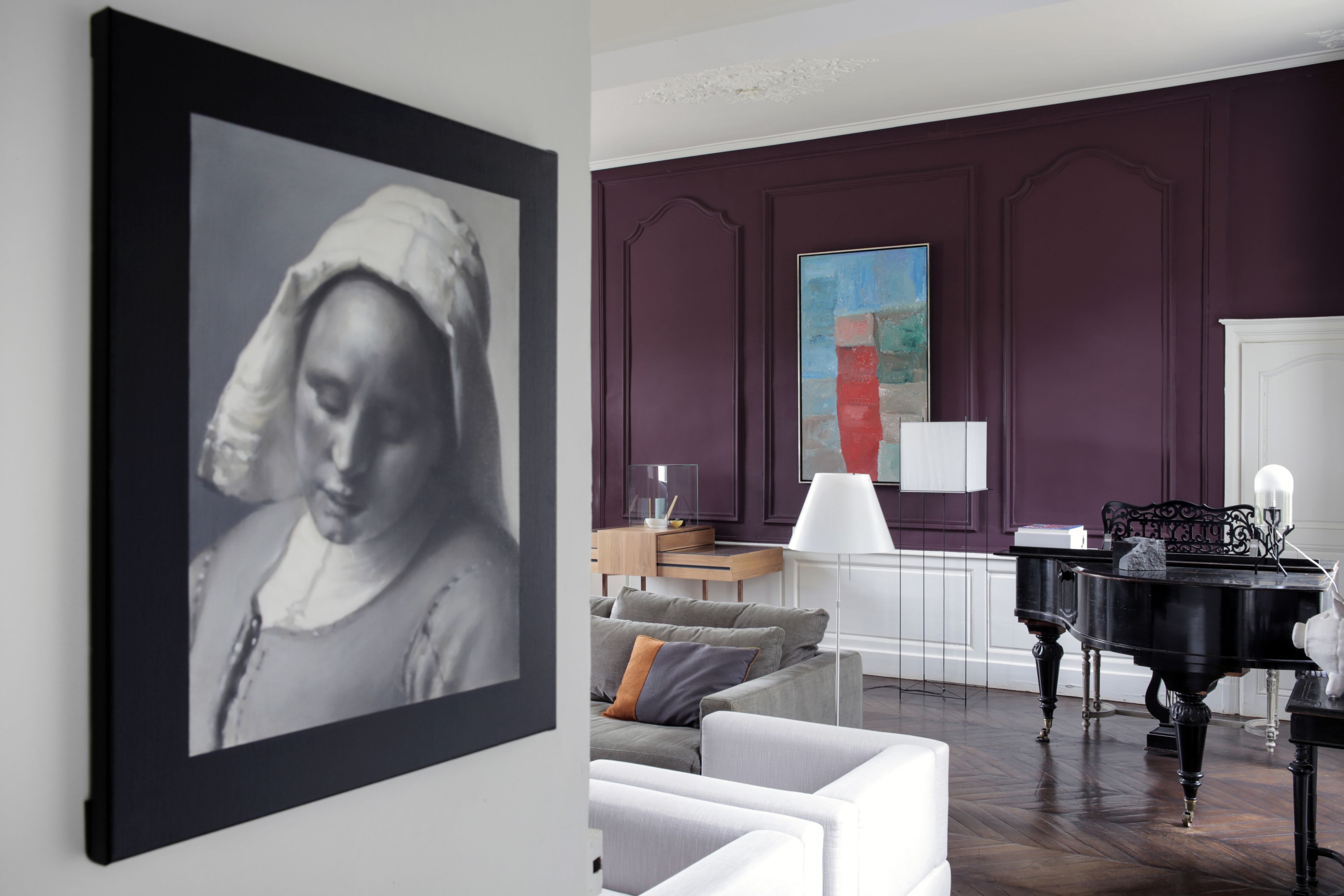 A living room with a framed black and white painting, a modern sofa, a piano, and a large abstract painting on the wall.
