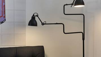 Une pièce moderne avec un lampadaire noir, un canapé foncé et une petite table d’appoint en bois sur laquelle se trouve un verre.