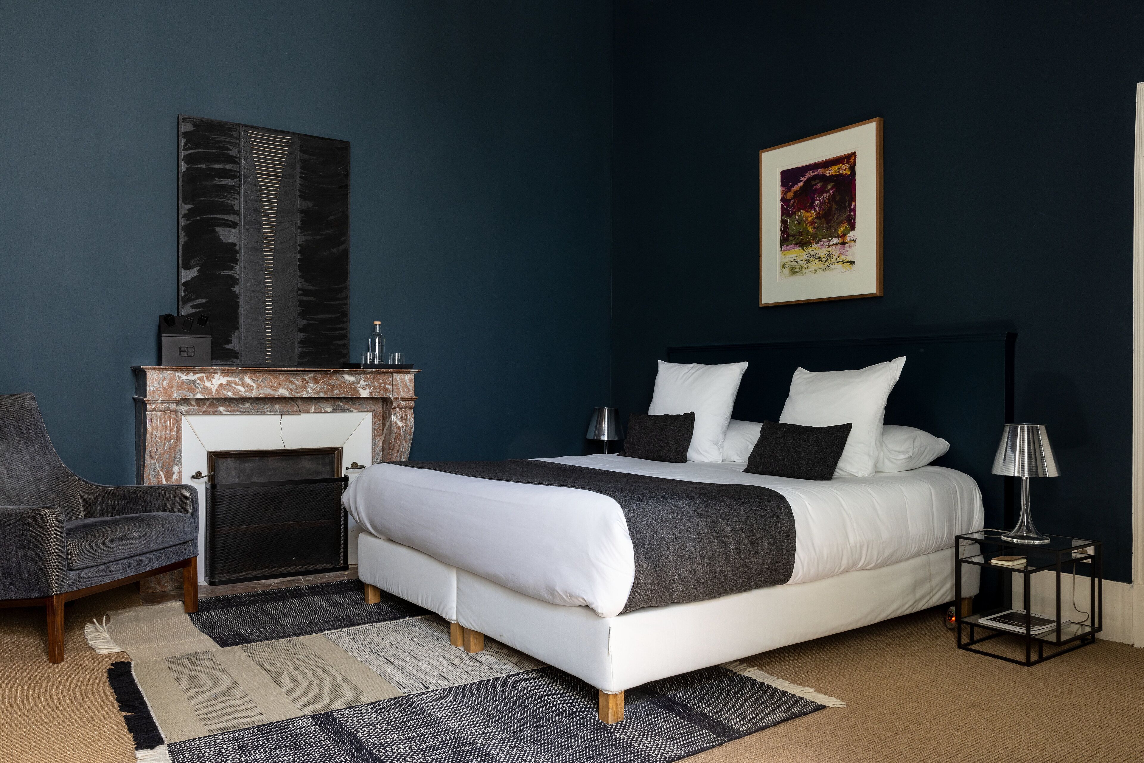 A bedroom with a bed, a chair, a fireplace, and a nightstand.