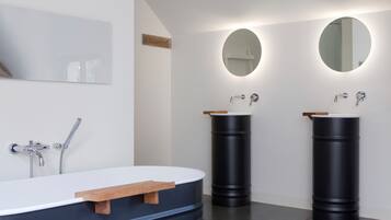 Une salle de bain moderne avec une grande baignoire, deux vasques avec des miroirs ronds et une étagère en bois.