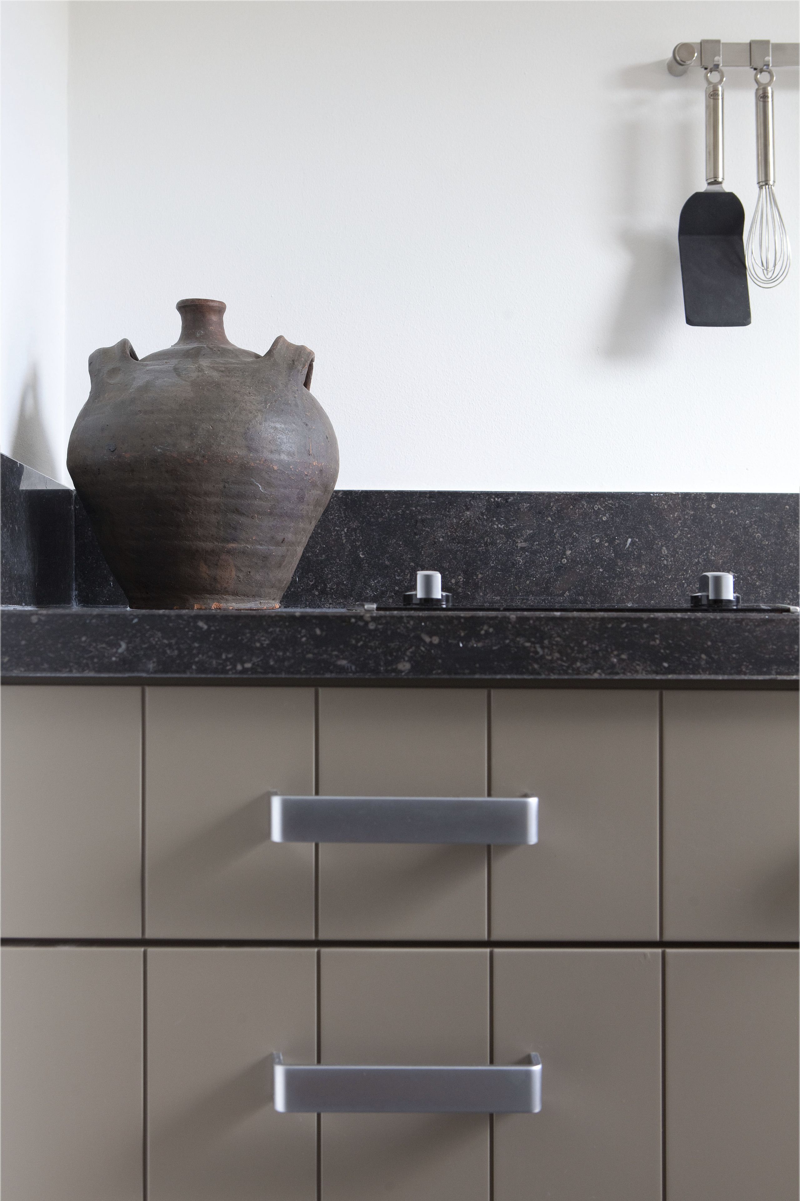 A kitchen with a large ceramic vase, a black countertop, and stainless steel handles on the cabinets.