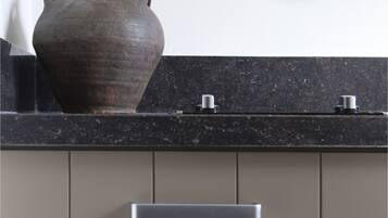 A kitchen with a large ceramic vase, a black countertop, and stainless steel handles on the cabinets.