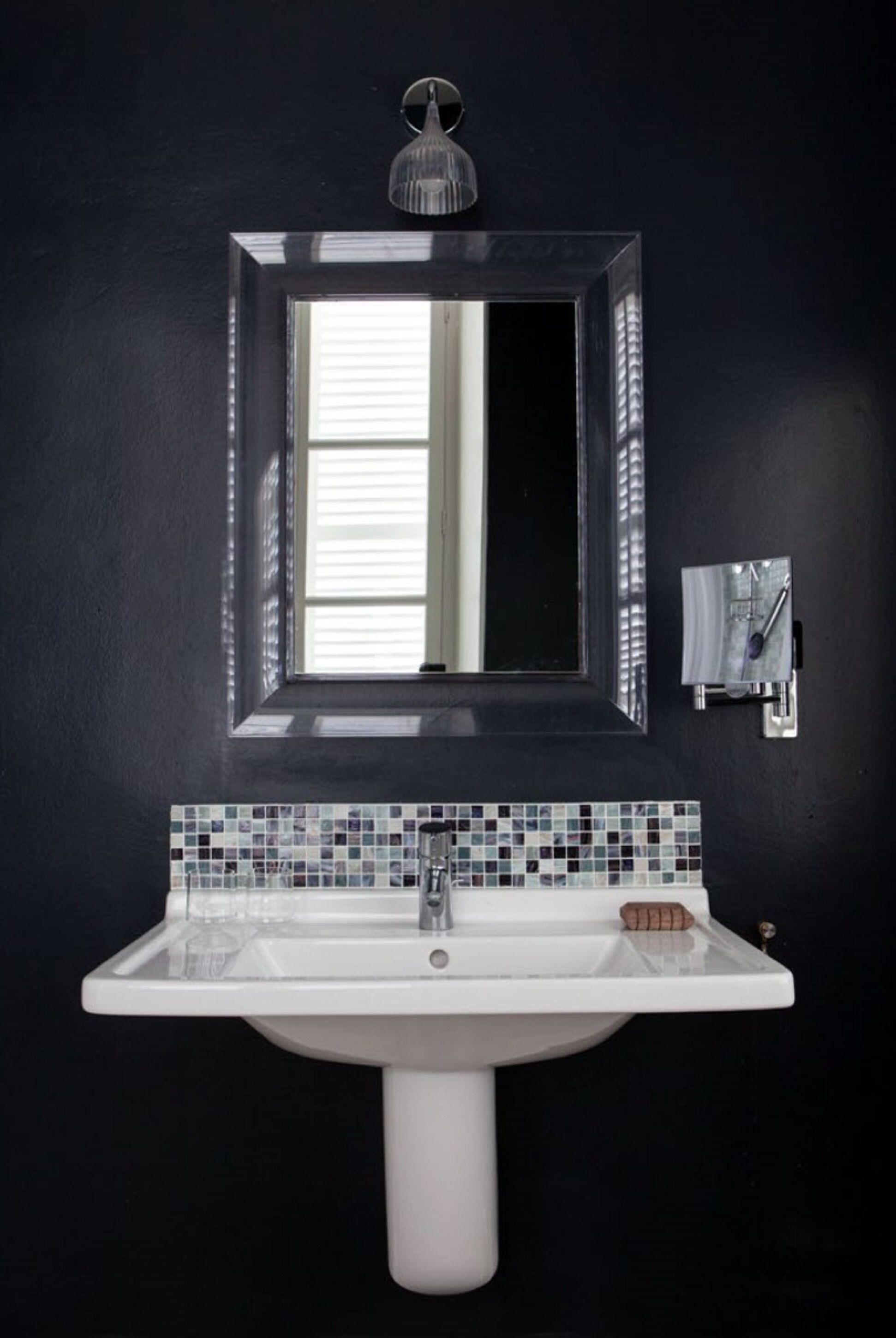 Un baño con un lavamanos blanco, un espejo y una ventana.