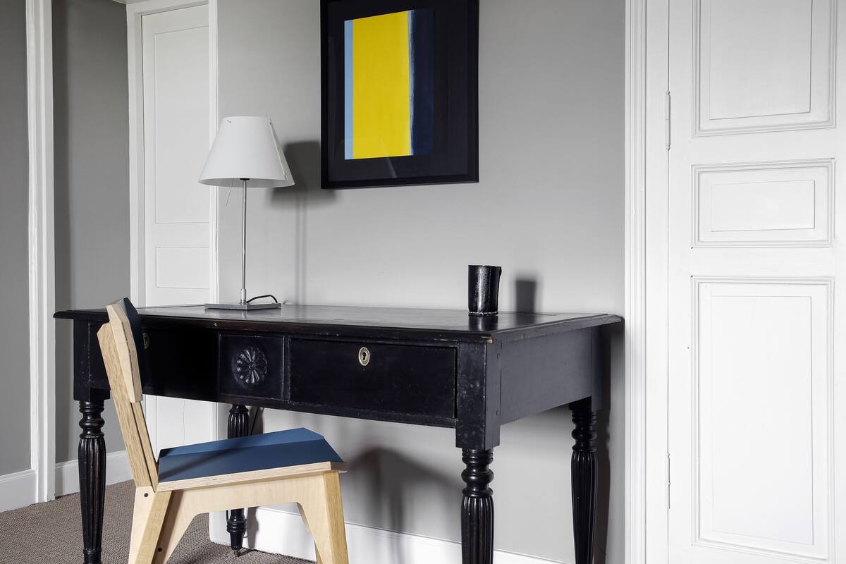 A black desk with a blue chair, a white lamp, and a framed picture on the wall.