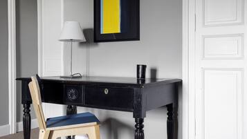 A black desk with a blue chair, a white lamp, and a framed picture on the wall.