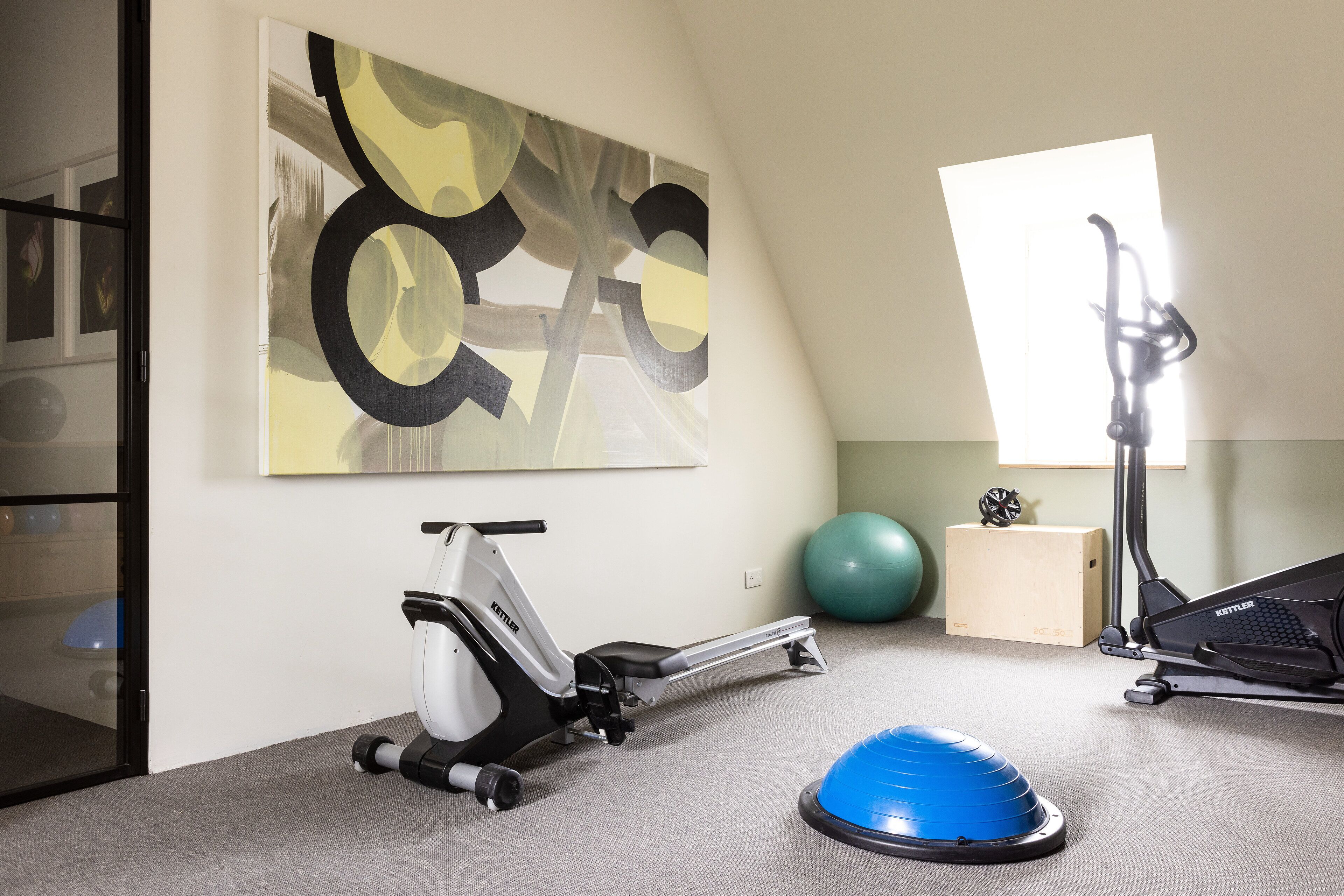 Une salle de sport à domicile équipée d’un vélo elliptique, d’un vélo d’appartement et d’un ballon d’exercice bleu.