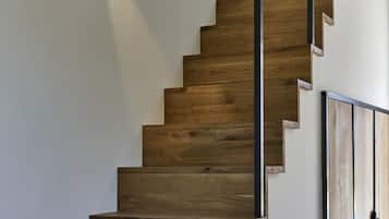 A wooden staircase with a modern design, featuring a metal handrail and a wall-mounted light fixture.